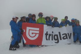 Mladi smučarji na snegu držijo transparent zavarovalnice Triglav
